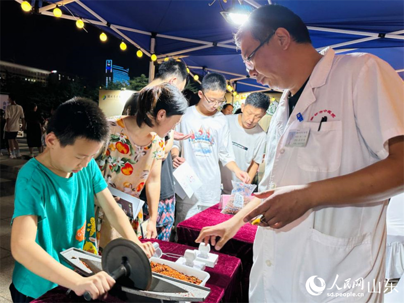 小學生在中醫(yī)藥文化夜市上研磨中藥粉。人民網 喬姝攝