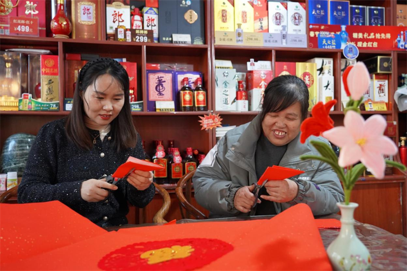 圖為張榮風(fēng)（左）與顧客共同制作新春剪紙