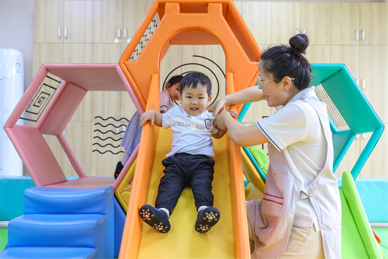 2025年5月14日，在山東省青島市李滄區(qū)職工子女愛心托育中心，小朋友在老師的陪伴下玩滑梯。張鷹 攝