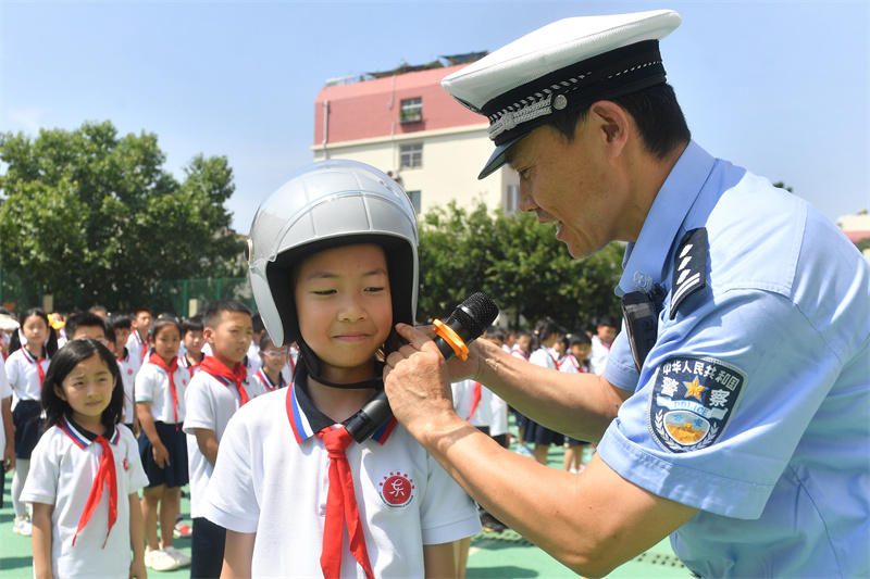 2025年7月4日，在山東省青島市市北區(qū)東勝路小學(xué)暑期休業(yè)式上，交警在指導(dǎo)學(xué)生正確佩戴安全頭盔。王海濱攝